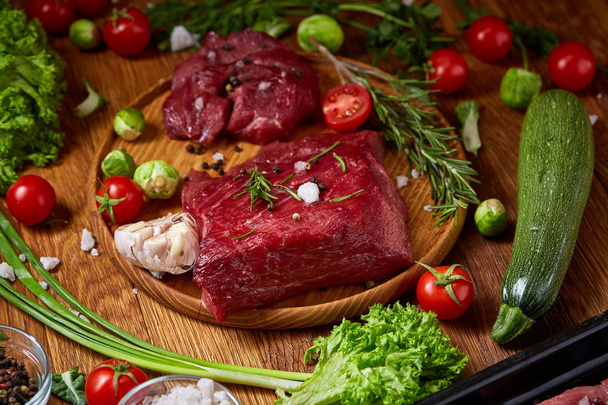 Still life of raw beef meat with vegetables on wooden plate over vintage background, top view, selective focus - Foto, Bild
