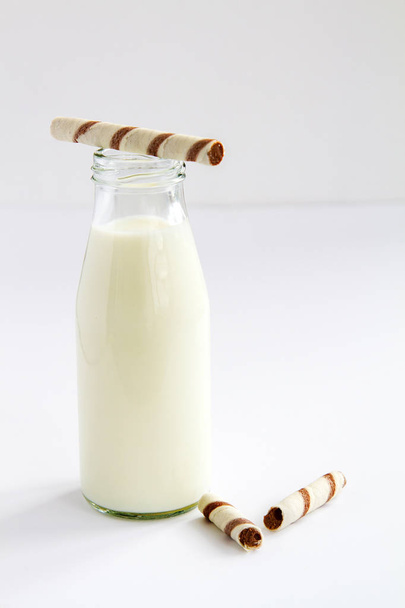 μπουκάλι γάλα δίπλα της σοκολάτα γκοφρέτα σωλήνες σε λευκό φόντο - Φωτογραφία, εικόνα
