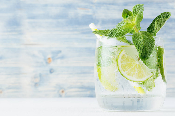 Fresh cold summer beverage with lime, leaf mint, straw, ice cubes on light blue wooden background, closeup. - Fotoğraf, Görsel