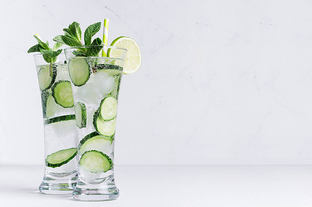 Fresh detox cocktail of cucumber, lime, mint, straw with bubbles, drops on soft white wooden backgrouns. Dieting spring cold drink. - Fotoğraf, Görsel