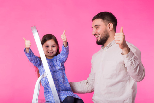 O pai e a filhinha com os polegares para cima sobre o fundo rosa. Homem adulto e bebê menina são felizes
 - Foto, Imagem