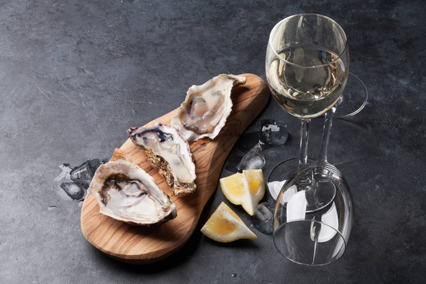 Otwarty ostrygi, lodu i cytryny i białe wino na stole z kamienia. Z miejsca kopii - Zdjęcie, obraz