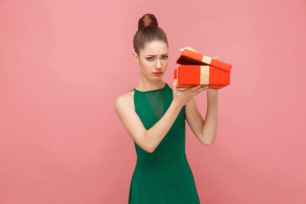 sad woman unboxing red gift box and looking inside on pink background - Foto, imagen
