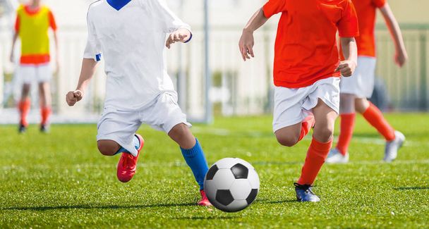 若いサッカー選手を実行します。フットボールを蹴る選手とのマッチゲームします。少年サッカーの選手がボールの後を実行しています。バック グラウンドでサッカー スタジアム。ピッチ上の少年がサッカーの試合 - 写真・画像