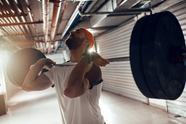 Молодой мускулистый человек делает высокотяговые упражнения с штангой на перекрестных тренировках
 - Фото, изображение