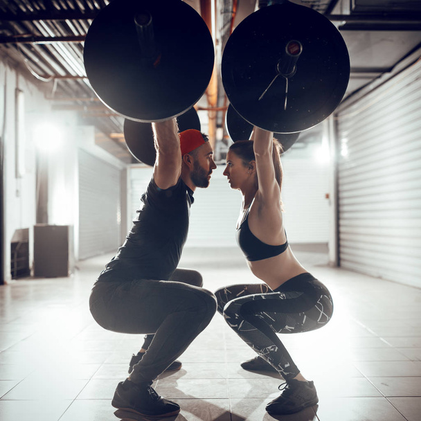 Giovane coppia muscolare che fa esercizio squat aerea con bilanciere su cross training
 - Foto, immagini