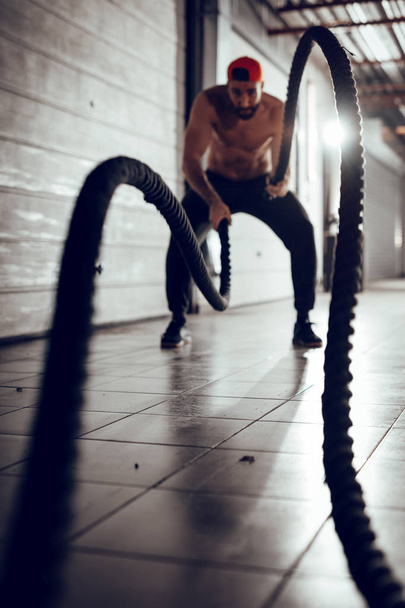 muscular young man exercising with ropes in garage gym - 写真・画像