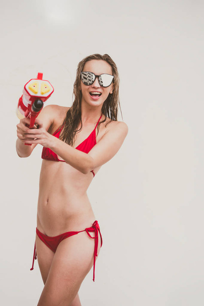 Attraktive junge Frau im roten Bikini mit Wasserpistole auf weißem Hintergrund - Foto, Bild
