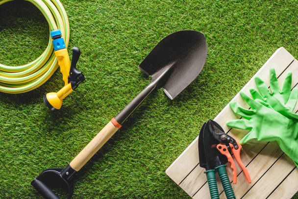 верхний вид шланга, защитные перчатки и садовые инструменты на траве
  - Фото, изображение