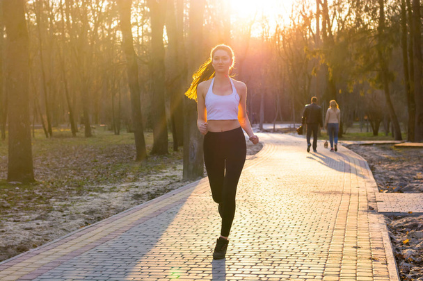 Young girl in headphones enjoys jogging in park at sunset - Photo, Image