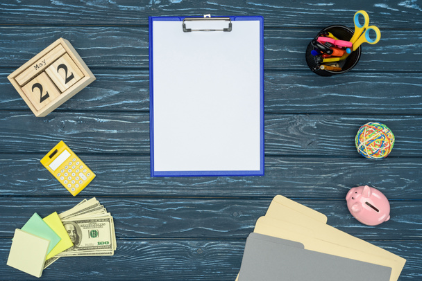 Бумага с чистой бумагой на синем деревянном столе с канцелярскими принадлежностями и деньгами
 - Фото, изображение