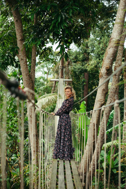 χαμογελώντας ελκυστική γυναίκα στέκεται στην πεζογέφυρα στη ζούγκλα και αναζητούν μακριά - Φωτογραφία, εικόνα