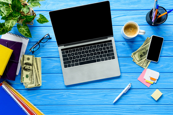 Laptop aberto em mesa de madeira azul com papelaria e dinheiro
 - Foto, Imagem