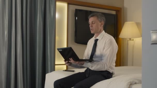 Biznesmen rozmawiasz za pośrednictwem laptopa w pokoju hotelowym - Materiał filmowy, wideo