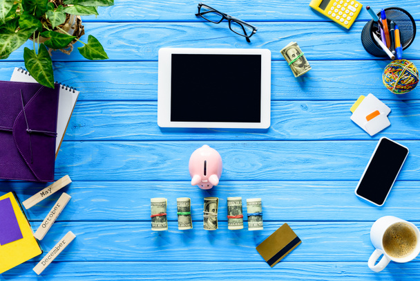  Digital tablet with piggy bank and money on blue wooden table - Fotoğraf, Görsel