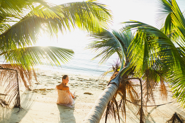 attractive woman sitting between palm trees on ocean beach - Photo, Image