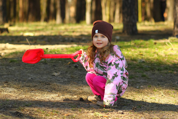 Cheerful todler girl showing the way in the forest with a red shovel - Foto, immagini