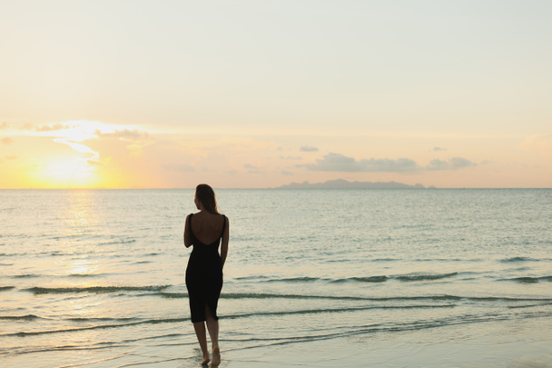 rear view of woman standing in ocean during sunset - Foto, afbeelding