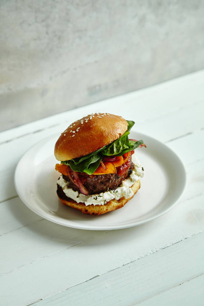 white ceramic plate with burger of grilled beef patty with cream cheese and spinach on classical bun on wooden table  - Foto, Imagem