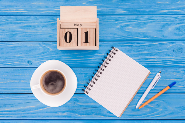 верхний вид деревянного календаря с датой 1 мая, чашка кофе, чистый учебник и ручки, концепция международного дня работников
  - Фото, изображение