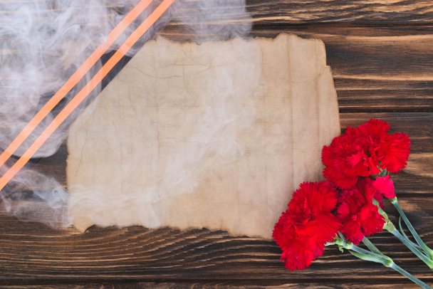 καπνίζετε πάνω από την κορδέλα του Αγίου Γεωργίου, παλιό άδειο χαρτί και γαρίφαλα σε ξύλινη επιφάνεια - Φωτογραφία, εικόνα