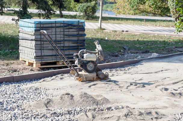 Vibrating plate compactor for sealing sand before laying tiles. Pallet with tiles on a city background. - Photo, Image
