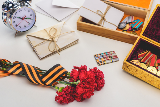closeup shot of carnations wrapped by st. george ribbon, letters, medals in boxes and alarm clock, victory day concept  - Zdjęcie, obraz