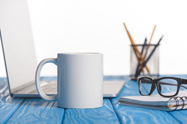 closeup shot of cup, eyeglasses on textbook, laptop and organizer with pens and pencils  - 写真・画像