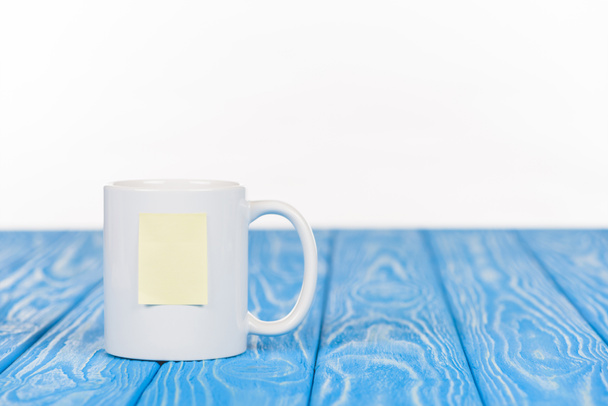 Nahaufnahme einer Tasse mit leerem Notizpapier auf blauer Holzoberfläche - Foto, Bild