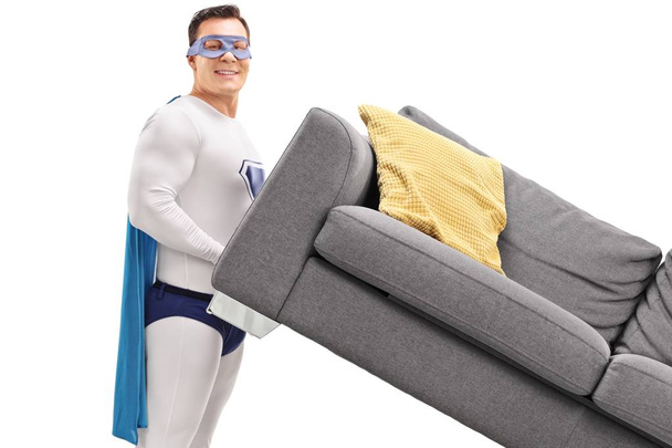 Man in a superhero costume lifting a sofa isolated on white background - Foto, imagen