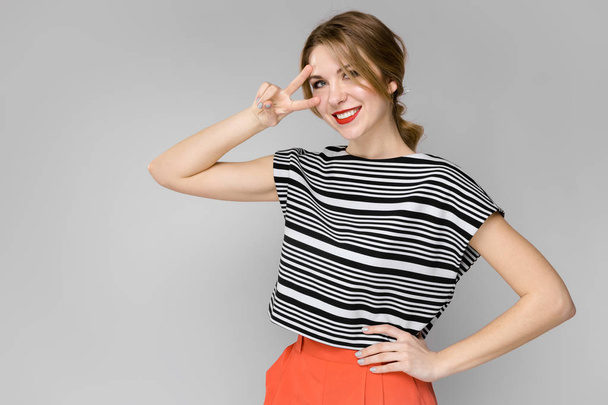 Atractiva joven mujer rubia caucásica en traje casual que muestra diferentes expresiones en la pared gris en el estudio
.  - Foto, Imagen
