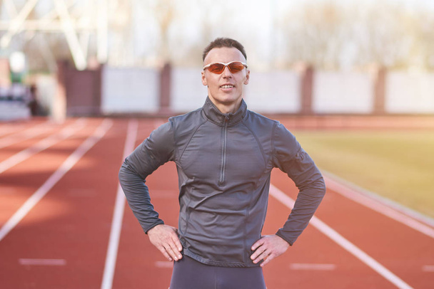Handsome athletic man posing on the running track of the stadium - Photo, Image
