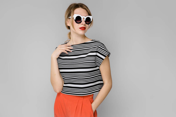 Atractiva joven mujer rubia caucásica en traje casual y gafas de sol que muestran diferentes expresiones en la pared blanca en el estudio
.  - Foto, Imagen