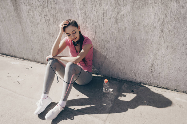 active sports girl is resting after a hard workout outdoors, sitting on the ground and gaining strength - Foto, Imagem