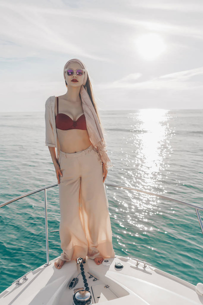 a luxurious young strong girl in sunglasses sails on her white expensive yacht on the Caribbean sea - Фото, зображення