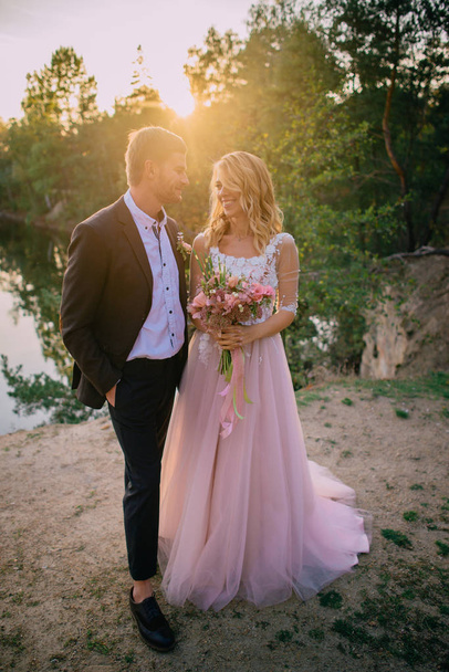 happy newlyweds standing on the lake shore at sunset - Foto, imagen