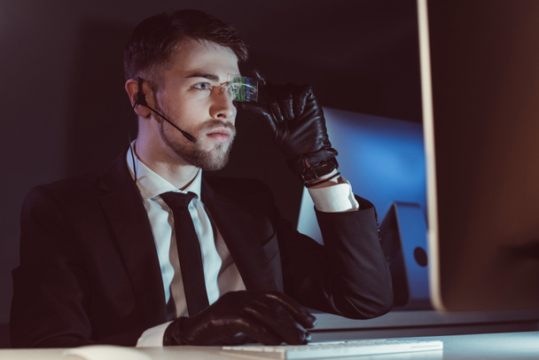 портрет хакера с гарнитурой, смотрящего на экран компьютера за столом в темноте
 - Фото, изображение
