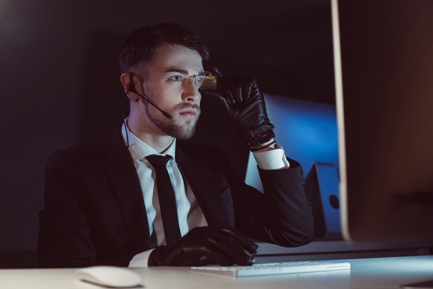 retrato de agente espía con auriculares mirando la pantalla de la computadora en la mesa en la oscuridad
 - Foto, imagen