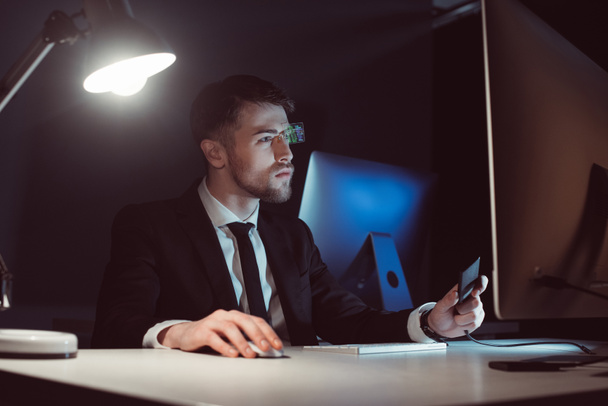 портрет хакера, який дивиться на екран комп'ютера за столом в темряві
 - Фото, зображення