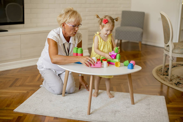 Бабушка играет с маленькой внучкой в комнате дома
 - Фото, изображение