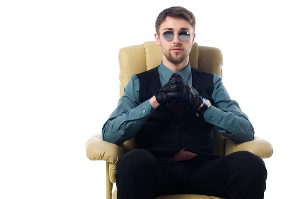 portrait of stylish spy in sunglasses and gloves sitting in armchair isolated on white - Foto, immagini