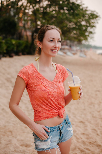 smiling attractive girl standing with cocktail on sandy beach and looking away - Foto, Bild