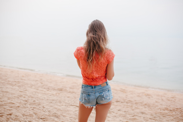 rear view of woman standing in shorts on sandy beach - Zdjęcie, obraz