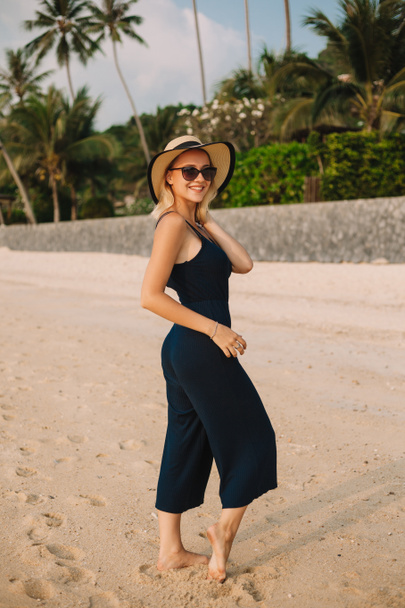 smiling attractive woman in hat standing on sandy ocean beach - Фото, зображення