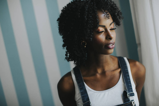 hübsche junge afrikanisch-amerikanische Frau posiert in Jeanshosen an der Wand im Zimmer - Foto, Bild