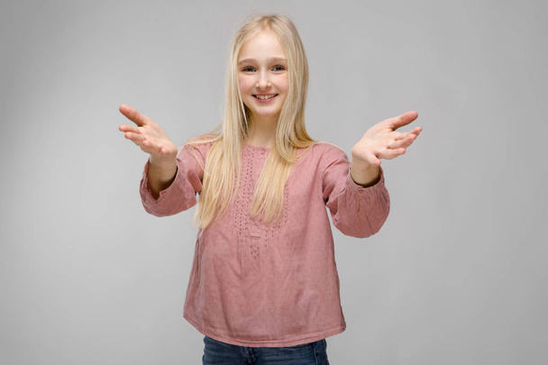 Αρκετά Καυκάσιος ξανθιά εφηβικό κορίτσι σε καρώ πουκάμισο και τα γυαλιά που παρουσιάζουν διαφορετικές συναισθηματικές εκφράσεις στον γκρίζο τοίχο στο studio. Εξάπλωση τα χέρια. - Φωτογραφία, εικόνα