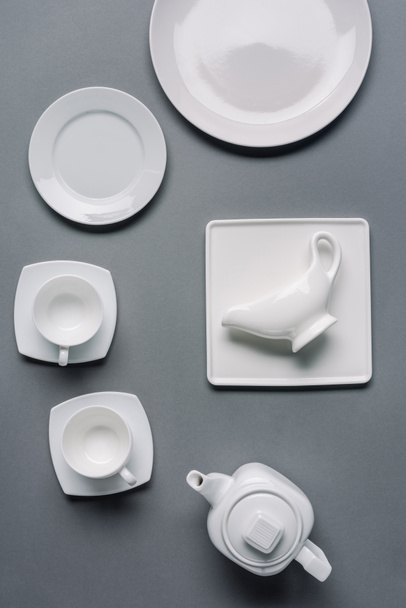 Çaydanlık ve bardak gri arka plan üzerinde beyaz tabaklar - Fotoğraf, Görsel