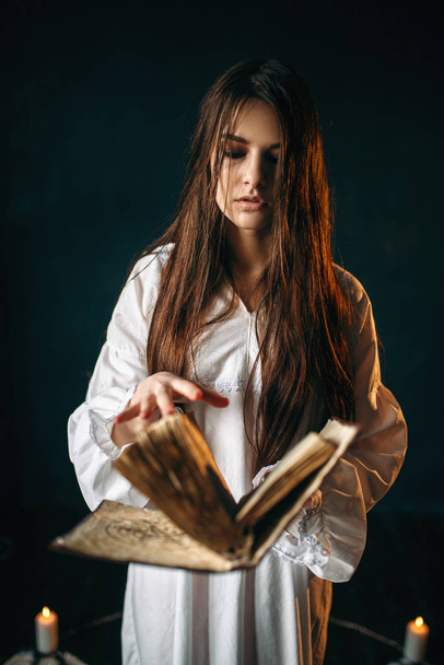 young woman in white shirt standing in the center of pentagram circle with candles and reading a spell, dark magic ritual, occultism - Valokuva, kuva