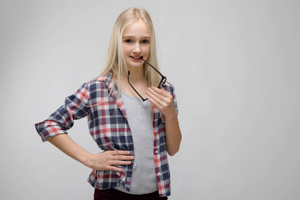 Pretty caucasian blonde teenage girl in checkered shirt and glasses showing different emotional expressions on grey wall in studio. - 写真・画像