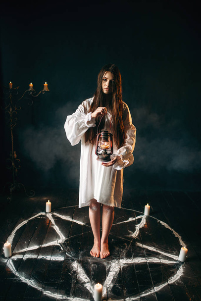 young woman holding kerosene lamp, pentagram circle with candles, black magic ritual, occult and exorcism - Photo, Image